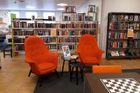 Interiör med två orange fåtöljer och bokhyllor på Hässelby villastads bibliotek